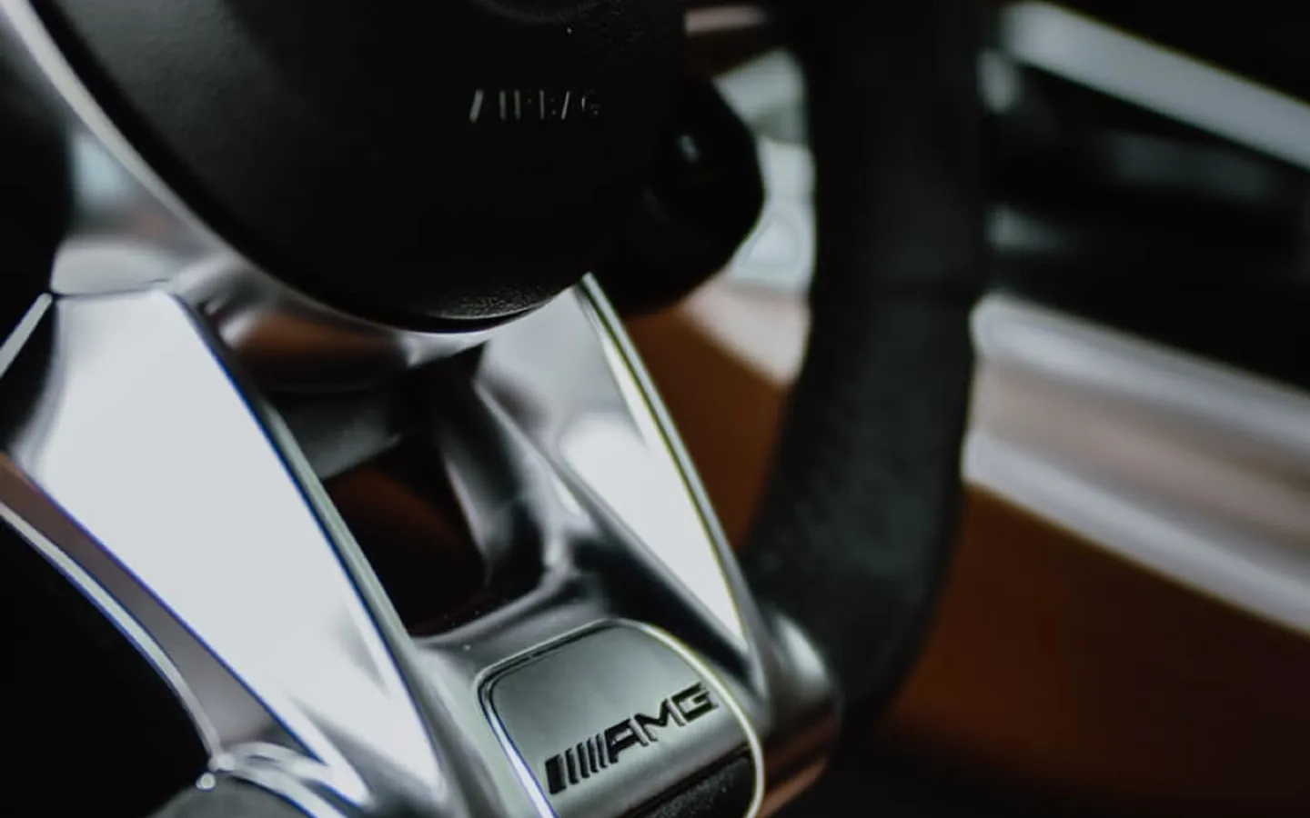 Close-up view of a Mercedes-AMG steering wheel, highlighting the metallic AMG badge and premium leather detailing.