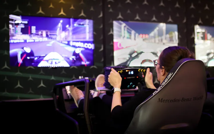 Visitor using a high-tech racing simulator at Mercedes-Benz World, engaging in a virtual Formula 1 driving experience with immersive screens and controls.