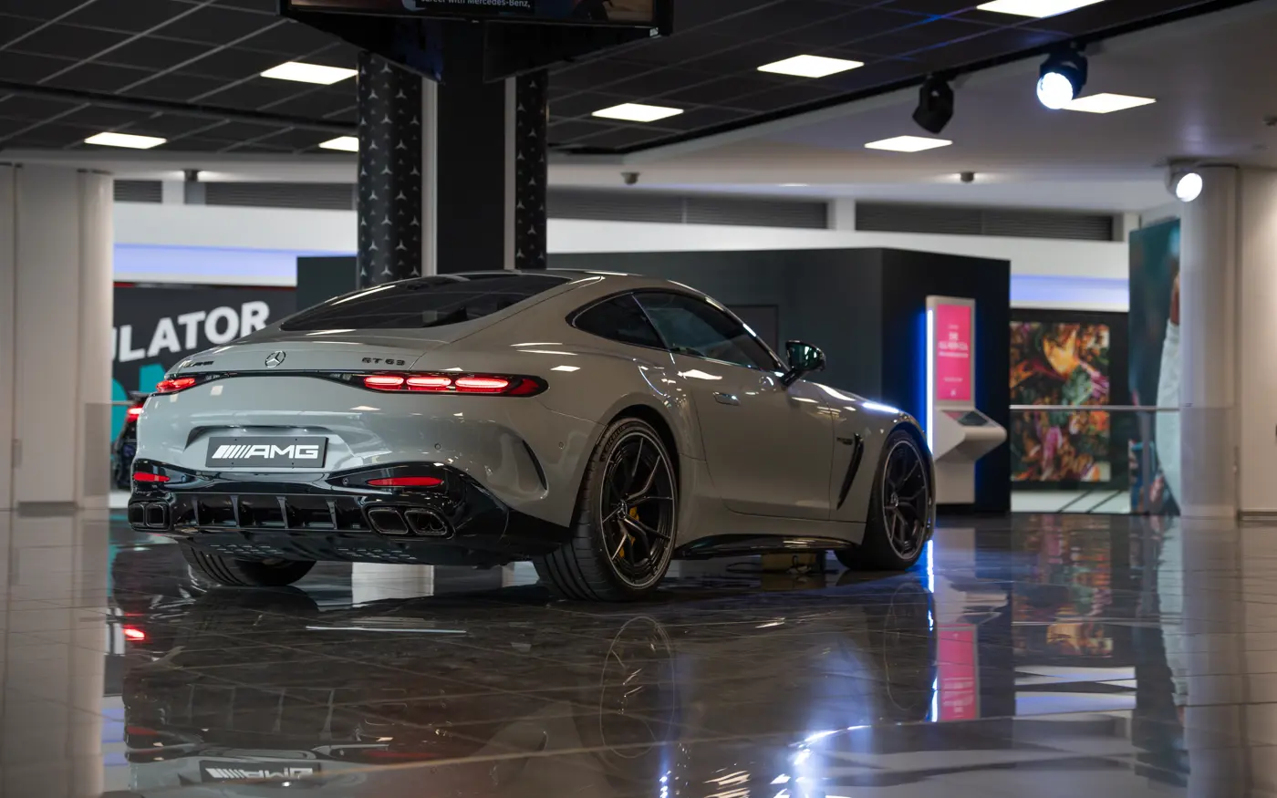 Rear view of a sleek Mercedes-AMG GT 63 showcased under showroom lighting at Mercedes-Benz World, emphasizing its sporty design and quad exhaust system.