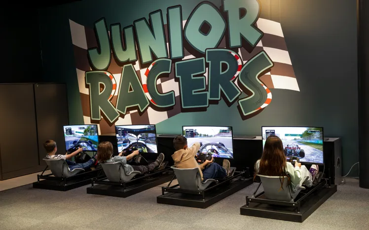 Children using racing simulators in the Junior Racers zone at Mercedes-Benz World, enjoying interactive motorsport experiences in a themed environment.
