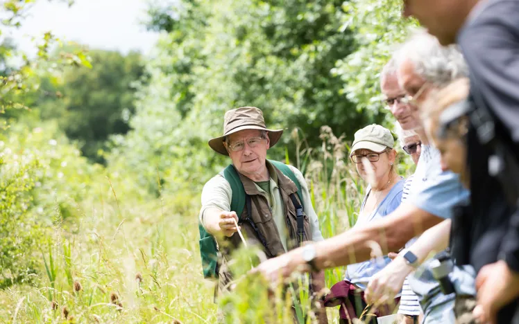 Volunteer leader at Heart of England Forest pointing out insects to visitors, promoting biodiversity education and conservation.